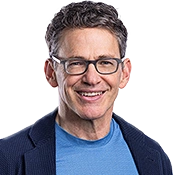 Section of an image featuring Bill Anderson in relief, wearing a light blue T-shirt, a blue blazer, and glasses, smiling at the camera.