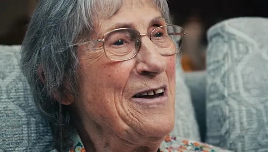 A woman in profile, wearing a colorful shirt, is looking out the window into the distance.