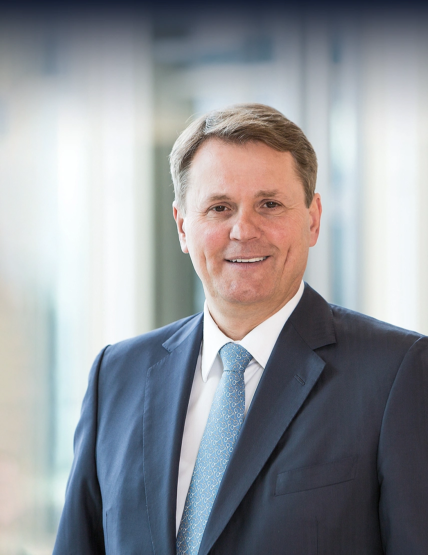 Norbert Winkeljohann is wearing a white shirt, a light blue tie, and a gray blazer, smiling at the camera.