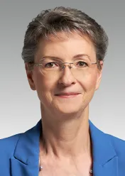 Heike Prinz trägt einen blauen Blazer und eine Brille und lächelt in die Kamera.