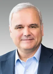 Stefan Oelrich trägt ein weißes Hemd und ein schwarzes Sakko und lächelt in die Kamera.